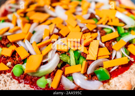 Makro Nahaufnahme von Hausgemachte warme Pizza mit Tomatensauce und Toppings grüne Paprika Zwiebeln gehackt und vegan Cheddar Stockfoto