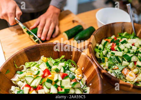 Schneidbrett mit Mann schneiden Gurken für Gemüse Salate in zwei Schüsseln mit vegan Römersalat Mittag- oder Abendessen am Küchentisch Stockfoto