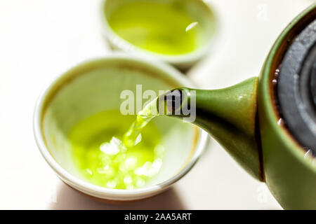 Nahaufnahme von grünem Ton Teekanne Teekanne auf weißem Hintergrund und gießt flüssige Bewegung der bunte lebendige Japanische Sencha oder genmaicha Getränk während Stockfoto