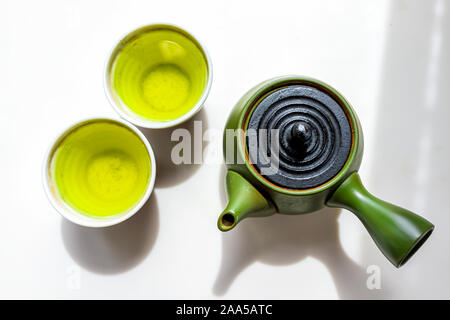 Grüner Ton Teekanne mit kyusu Griff oben flach Flach Blick hinunter auf weißem Hintergrund Zähler mit Japanischen Tee genmaicha oder Sencha in cups Duri Stockfoto