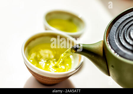 Grüner Tee Ton Teekanne auf weißem Hintergrund und gießt flüssige Bewegung von bunten Gelb oder japanischen Sencha genmaicha Trinken während der Zeremonie Stockfoto