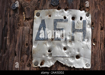 Metallische tag auf hölzernen Lamp Post mit den Initialen der griechischen öffentlichen Stromversorger genagelt. Stockfoto