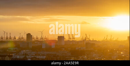 Krane und Windkraftanlagen bei Sonnenuntergang in der Hafengegend von Hamburg, Deutschland. Stockfoto