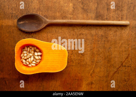 Halb reifer Butternusskürbis mit Samen und altem Holzlöffel auf rustikalem Holztisch Stockfoto