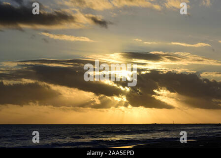 Dramatischer Sonnenuntergang vor Wolkenhimmel am Meer an der Küste mit Wasser und Wellen als Hintergrund Stockfoto