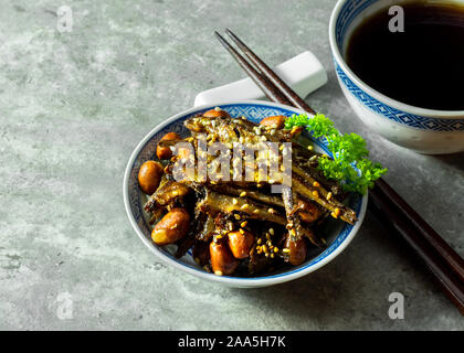 Tazukuri, kandierte Sardinen mit einem heißen steilen schwarzen Tee serviert. Getrocknete Sardinen leicht mit Honig, geröstetem Sesam und Erdnüsse. Stockfoto