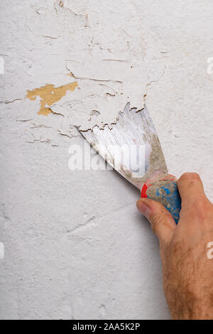 Entfernen alter Farbe von der Wand mit einem Metallspachtel. Kleine Malerarbeiten zu Hause. Hellen Hintergrund. Stockfoto