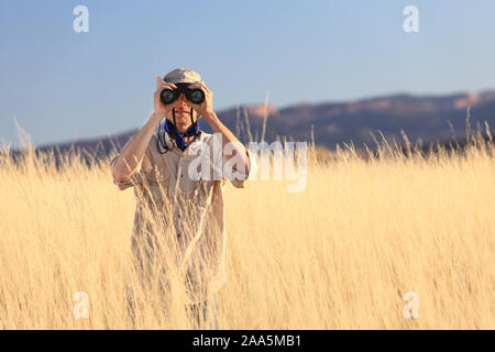 Safari Mann schaut durch ein Fernglas im langen Gras Stockfoto