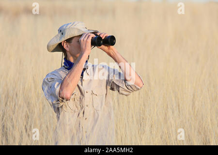 Safari Mann schaut durch ein Fernglas im langen Gras Stockfoto