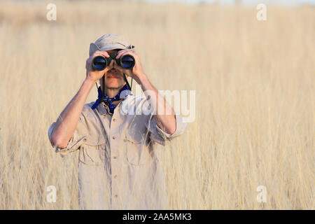 Safari Mann schaut durch ein Fernglas im langen Gras Stockfoto