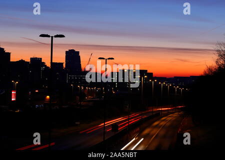 Leeds Skyline bei Sonnenaufgang mit leichten Wanderwegen vom Verkehr auf der Canal Street in Armley. Stockfoto