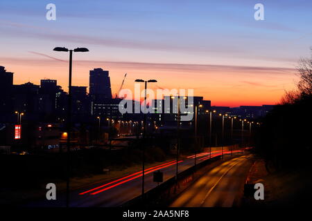 Leeds Skyline bei Sonnenaufgang mit leichten Wanderwegen vom Verkehr auf der Canal Street in Armley. Stockfoto