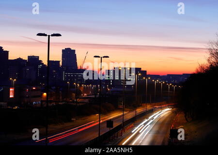 Leeds Skyline bei Sonnenaufgang mit leichten Wanderwegen vom Verkehr auf der Canal Street in Armley. Stockfoto