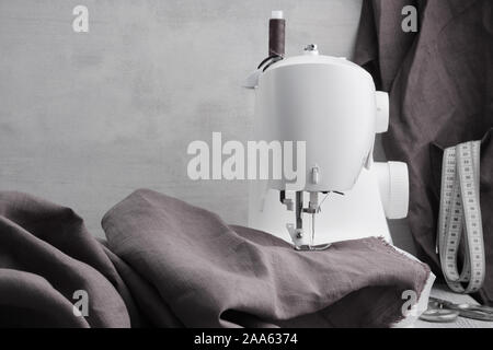 Nähen leinene Kleider auf einer Nähmaschine. Im Hintergrund ist eine hängende Leinen Schürze mit einem Maßband in der Tasche. Der Workshop anpassen. Stockfoto