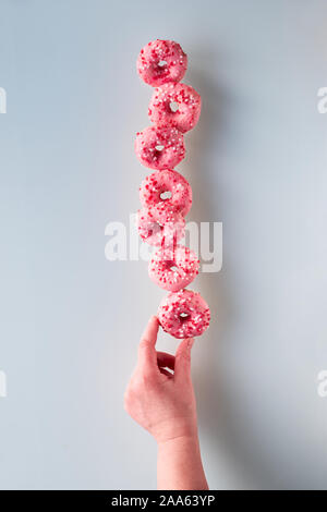 Kreative Bild der vollkommenen Balance, Turm oder der Pyramide von leckeren Rosa donuts Balancieren auf der Unterseite Donut in der Hand hielt. Beliebte hanuka Dessert. Stockfoto