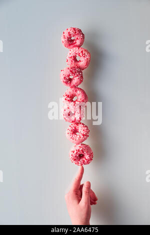 Kreative Bild der vollkommenen Balance, Turm oder der Pyramide von leckeren Rosa donuts Balancieren auf Zeigefinger, weibliche Hand. Beliebte chanukah Dessert. Konzeptionelle e Stockfoto