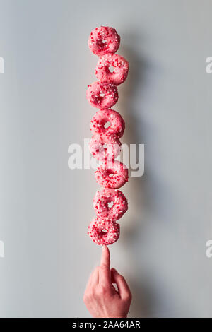 Kreative Bild der vollkommenen Balance, Turm oder der Pyramide von leckeren Rosa donuts Balancieren auf Zeigefinger der Hand. Beliebte chanukah Süßigkeiten. Konzept Stockfoto