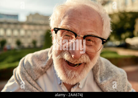Nicht über älter zu machen. Portrait von gut aussehenden Bärtigen älteren Mann in Gläsern an Kamera schauen und lächeln beim Stehen im Freien an einem sonnigen d Stockfoto