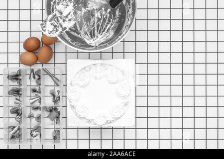 Backen Werkzeuge im Mixer Schüssel nach Kuchen Glasur, rohe Eier und eine Schachtel mit Düsen auf flache weiße überprüft Hintergrund legen Stockfoto