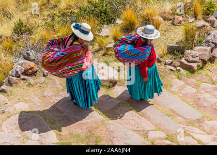 Zwei Quechua indigene Frauen in traditioneller Kleidung und Textilien zu Fuß die Schritte auf der Insel Taquile am Titicacasee, Puno, Peru. Stockfoto