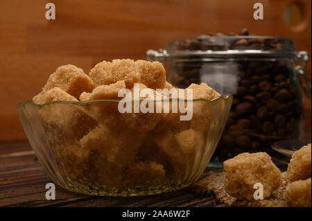 Stücke von braunem Zucker in einer Schüssel Zucker und Kaffee Bohnen im Glas auf einer hölzernen Hintergrund. Nahaufnahme Stockfoto