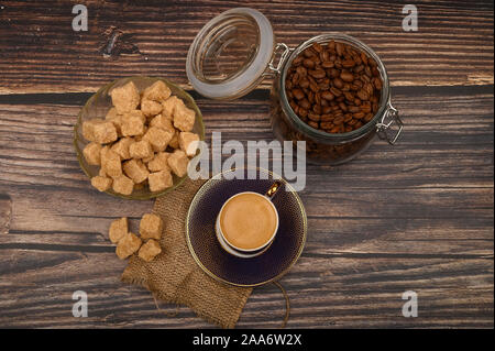 Eine Tasse Kaffee, Kaffeebohnen im Glas und Stücke von braunem Zucker auf einer hölzernen Hintergrund Stockfoto
