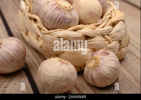 Ein paar Köpfe junger Knoblauch in einem Weidenkorb auf einer hölzernen Hintergrund. Herbst Ernte. Die moderne Landwirtschaft. Nahaufnahme Stockfoto