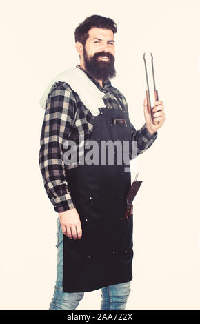 Seine Hand fern von Flamme. Der bärtige Mann mit Grill Zange in den Händen. Grill kochen mit Küche Zange. Koch hipster Holding Edelstahl Zange. Kochen Zangen für die Zubereitung und Servieren von Speisen. Stockfoto