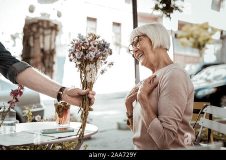 Freudige schön gealterte Frau mit schönen Blumen Stockfoto