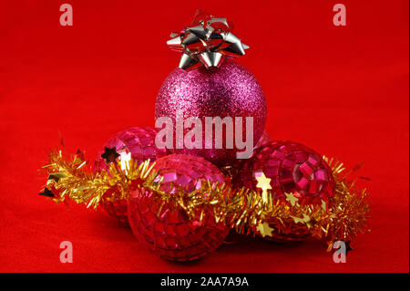 Lila und rosa runde Christbaumkugeln mit einem silbernen Stern auf Gold und lametta vor Stockfoto