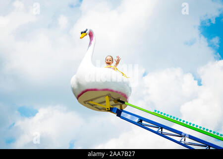 Glückliches Mädchen reiten auf einem hohen bunten Karussell während sonniger Tag im Vergnügungspark. Stockfoto