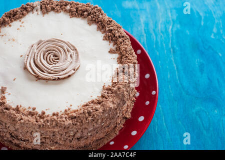 Schokoladenkuchen mit Sahne auf der roten Platte, blauer Hintergrund Stockfoto