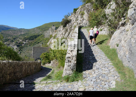 Touristen oder Besucher zu Fuß auf befestigten Pfad oder im Zickzack von Mauern umgebene Wanderweg führt von Entrevaux Dorf an der Zitadelle Provence Frankreich Stockfoto