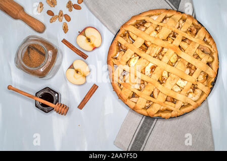 Apfelkuchen auf einem grauen Handtuch für die Küche, mit Äpfeln, Zimt, Zucker und Nüsse, Ansicht von oben Stockfoto