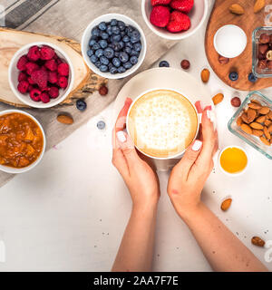 Guten Morgen - gesundes Frühstück Hintergrund mit Haferflocken Kaffee, Beeren, Ei, Nüsse. Kaffee, Hände, Halten, Schale. Weiß Holz- essen Hintergrund Stockfoto