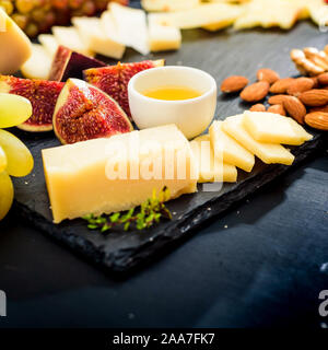 Käseplatte. Sortiment von Käse mit Walnüssen, Mandeln, Trauben, Feigen und Erdbeeren, Heidelbeeren und Honig Stockfoto