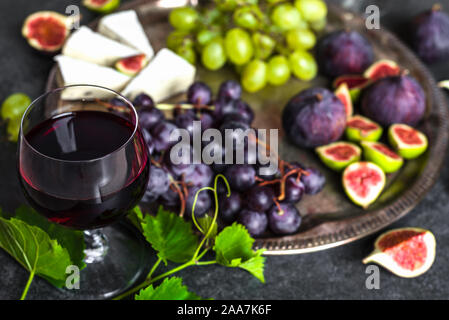 Glas Rotwein mit Käse, Weintrauben und Feigen. Französisch Essen am Plattenteller. Stockfoto