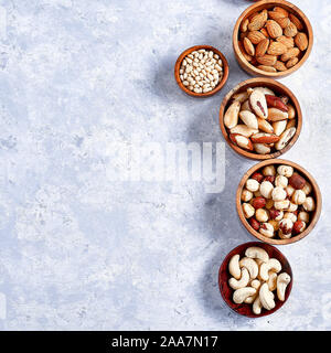 Eine Vielzahl von Nüssen, Mandeln, Walnüsse, Cashewkerne, Paranüsse, Haselnüsse, Pinienkerne in hölzernen Schüsseln auf einer blauen Tabelle Stockfoto