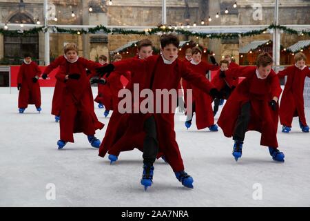 Winchester, Hampshire, UK. 20. November 2019. Chorknaben Schlittschuhlaufen auf der Eisbahn in ihrer berühmten roten Roben an der Winchester Cathedral als Weihnachtsfeier erhalten unterwegs mit der festliche Tradition der Vorsänger Skaten rund um die Eisbahn vor seiner Eröffnung morgen. Credit: Carolyn Jenkins/Alamy leben Nachrichten Stockfoto