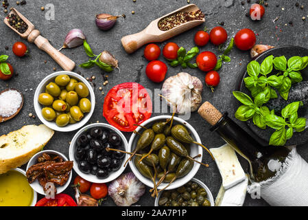 Mediterrane Küche auf dunklem Hintergrund: Kräuter, Oliven, Öl, Tomaten, Brot, Käse und Wein aus der Flasche. Stockfoto