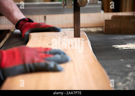 Tischler Schneiden von Holz Planke mit einer Bandsäge in Nahaufnahme auf der Klinge und seine behandschuhten Hände Stockfoto