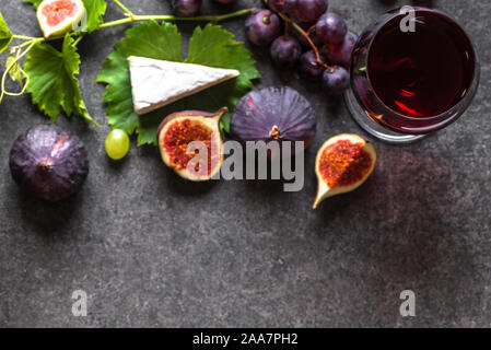 Glas Rotwein und Häppchen: französischer Käse, Feigen, Trauben. Stockfoto