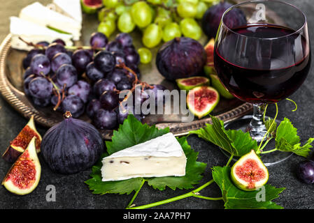 Französische Küche. Glas Rotwein und Snack, Platte mit Käse, Weintrauben und Feigen. Stockfoto