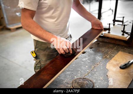 Tischler oder Schreiner Färbung oder Färbung eine briar root-Panel in Nahaufnahme auf der Planke des Holzes und seine Hände über die Workbench Stockfoto