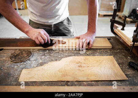 Zimmermann die Beize zu einem briar root-Panel auf einer Werkbank in einem Holzbearbeitung Workshop in einem niedrigen Winkel Blick auf seine Hände, als er Werke Stockfoto