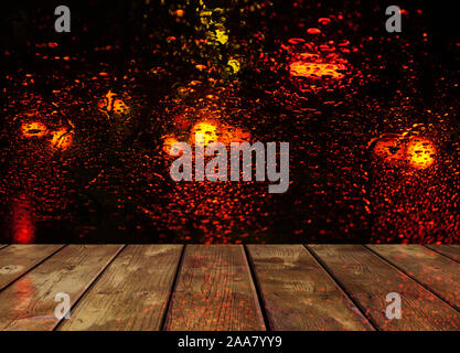 Regen fällt auf Glas Oberfläche mit roten bokeh Nacht die Lichter der Stadt mit Holztisch Stockfoto