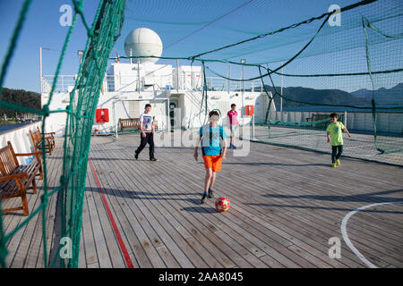 Jungen Fußball spielen auf dem Oberdeck eines großen Kreuzfahrtschiffes mit schützenden Verrechnung der Kugel zu enthalten. Stockfoto