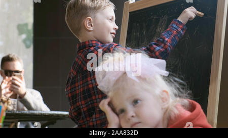 Close-up Bruder zieht mit Kreide an die Tafel. Stockfoto