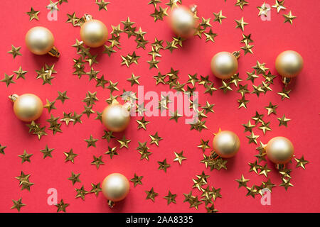Goldene Kugeln und Sterne glitter Konfetti auf rotem Hintergrund. Party Urlaub Kulisse. Ansicht von oben, flach Stil. Stockfoto