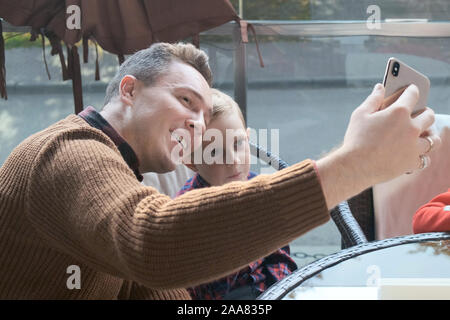 Familie in einem Café auf der Terrasse. Papa nimmt eine selfie mit seinem kleinen Sohn Stockfoto